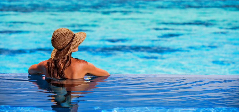 woman in straw hat resting at the edge of an infinity pool overlooking the sea